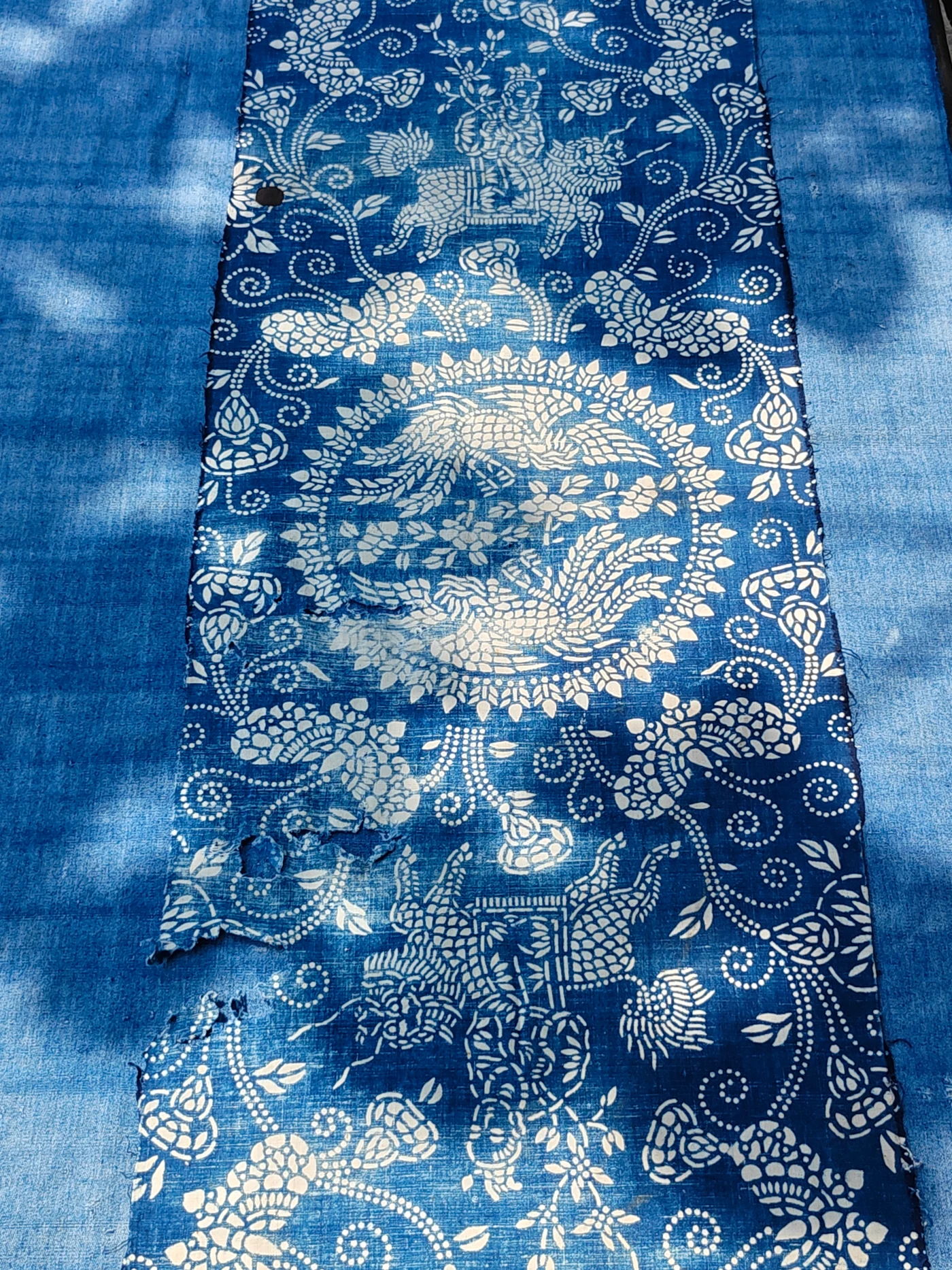 Wider view of the same worn textile: a child on a qilin, a phoenix medallion, surrounding motifs and areas of fabric loss.